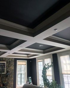 a living room with black walls and white trim on the ceiling, along with two windows