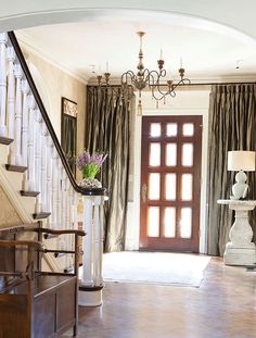 an entry way with a chandelier, vases and flowers on the table