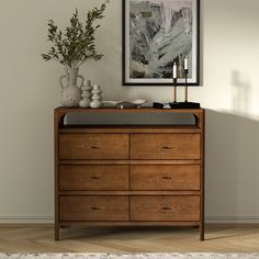 a wooden dresser sitting in front of a painting on the wall next to a potted plant