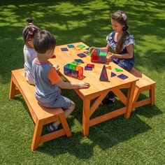 three children sitting at a picnic table playing with blocks