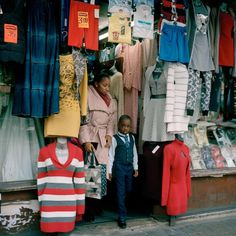 a woman standing next to a child in front of a clothing store with clothes on display