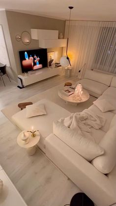 a living room filled with white furniture and a flat screen tv mounted on the wall