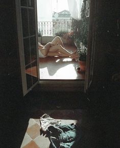 a naked woman laying on the floor in front of an open door to a balcony