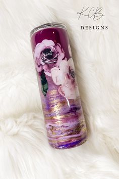 a purple and white flower painted on the side of a tumbler cup sitting on top of a furry surface