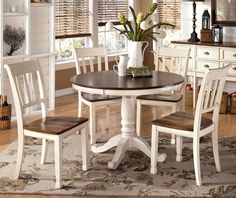 a dining room table with four chairs and a vase on top of it in front of a window