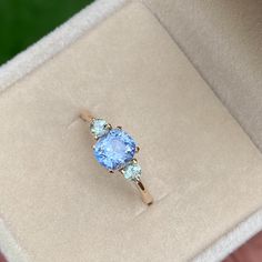 an engagement ring in a box with a blue topazte and green diamonds on it