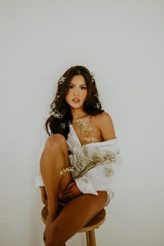 a woman sitting on top of a wooden stool wearing a white dress and flowers in her hair