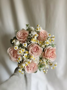 a bouquet of pink roses and daisies on a white cloth covered background with copy space