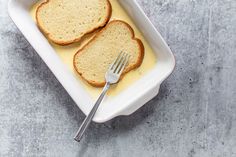 two slices of bread are in a white dish with butter and a fork on the side