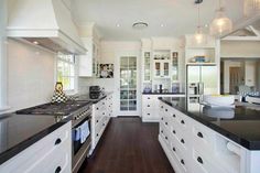 a large kitchen with white cabinets and black counter tops, along with dark wood flooring