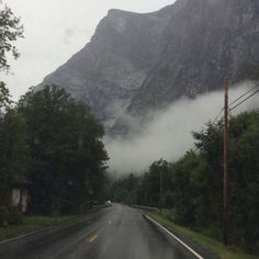 the mountains are covered in fog and low lying clouds as cars drive down the road