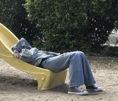 a person laying on a yellow slide in the dirt next to some bushes and trees