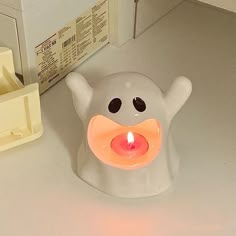 a white candle holder with an orange light in the shape of a ghost