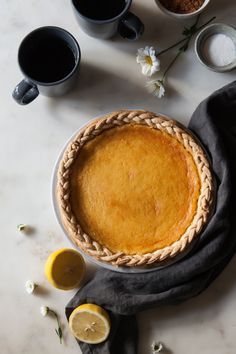 a pie sitting on top of a white table next to cups and lemon wedges