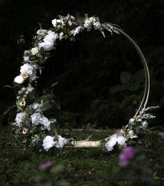 a circular wreath with white flowers and greenery on the ground in front of trees