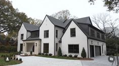 a large white house with black roofing and two car garages on the driveway