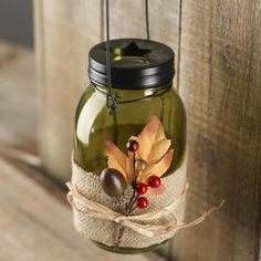 a green mason jar with fall leaves and berries on it hanging from a wooden fence