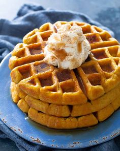 a stack of waffles on a blue plate topped with whipped cream and syrup