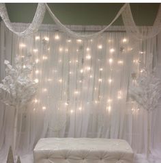 a white bench sitting in front of a window covered with curtains and fairy light garlands