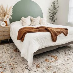 a bed with white sheets and pillows in a bedroom next to a dresser, rug and window