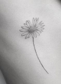 a small daisy tattoo on the back of a woman's stomach, with a thin line drawing of a single flower