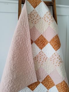 a pink and gold quilt on top of a wooden chair next to a white wall