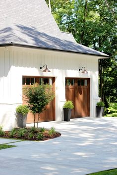 two brown garage doors on the side of a white building with trees in the background