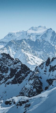 a man riding skis down the side of a snow covered mountain slope with mountains in the background