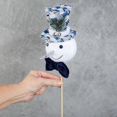 a hand holding a small white and blue hat on top of a toothpick