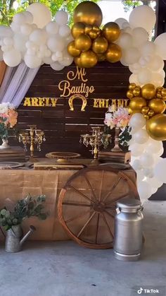 the table is set up with gold balloons and white streamers, as well as an old wagon