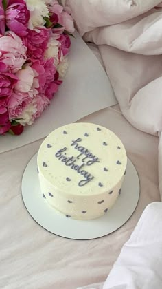 a birthday cake sitting on top of a white plate next to pink and white flowers