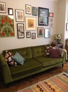 a green couch sitting in front of a wall filled with pictures and framed art on it