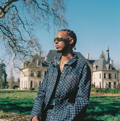 a man with dreadlocks standing in front of a large house on a sunny day