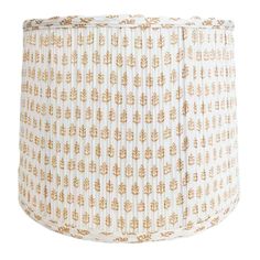 a white lamp shade with gold leaf print on the top and bottom, in front of a