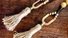 two wooden beads and tassels hang from hooks on a wood surface with the words,