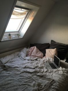 a laptop computer sitting on top of a bed under a slanted skylight in a bedroom