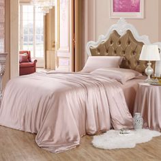 a bed with pink sheets and pillows in a room next to a chair, table and lamp