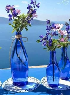 two blue vases with flowers in them sitting on a table next to the ocean