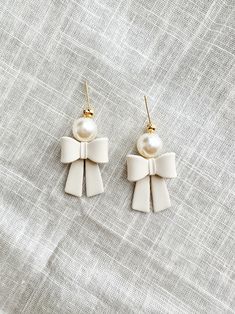 two pairs of earrings with white bows and pearls hanging from them on a gray cloth