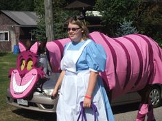 a woman in costume standing next to a car with a pink cat on it's back