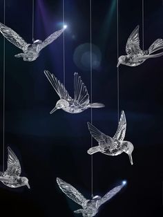 several glass birds hanging from strings in the air with lights shining behind them on a dark background