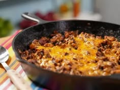 a skillet filled with cheese and meat on top of a table next to a fork