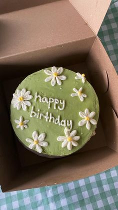 a green birthday cake in a box with daisies on the top and happy birthday written on it