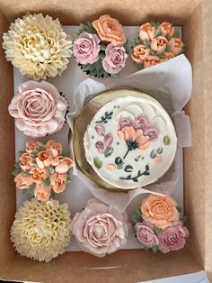 a box filled with cupcakes covered in frosting and decorated with pink flowers