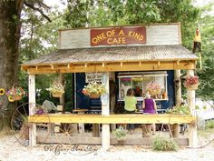 two people are sitting at the front of a small cafe with flowers in pots on the porch