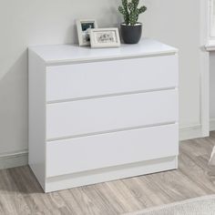 a white dresser with two drawers and a potted plant next to it on top