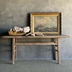 an old wooden table with flowers on it and a painting in the corner next to it