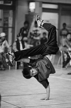 a man is doing a handstand on the ground while people watch in the background