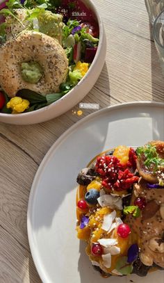 two plates filled with food on top of a wooden table next to a bowl of salad