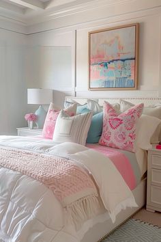 a white bed topped with lots of pillows next to a painting on the wall above it